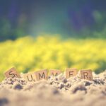 Scrabble tiles forming the word 'summer' in sand with a blurred background, evoking warm vibes.