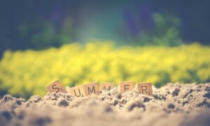 Scrabble tiles forming the word 'summer' in sand with a blurred background, evoking warm vibes.